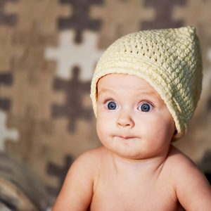 Little Newborn baby with big eyes hat knitting on a plain background