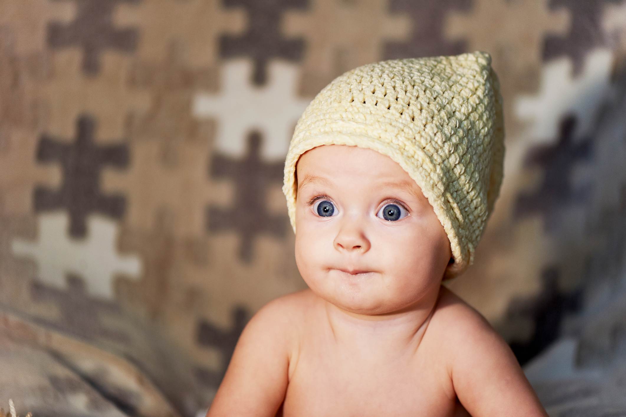 Little Newborn baby with big eyes hat knitting on a plain background